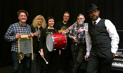 Second Wind Jazz Band vid inspelningen i Ålands Radios studio 4 januari 2018. Daniel Johansson (tvättbräda), Inger Marie Sundblom (trumpet), Sofia Enros (bastrumma), Marcus Qvarnström (gitarr, sång), Lillebror Lillis Börje Åhlund (klarinett), Andreas Karlsson (piano). Vid fototillfället närvarade ej den sjunde bandmedlemmen Ilse Enros (kazoo, äggmaracca, tvättbräda) Hot Jazz Mariehamn Åland